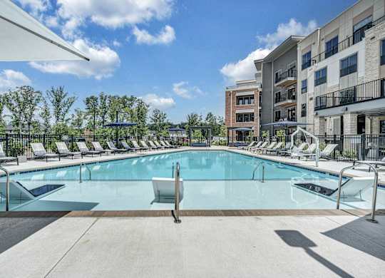 A large swimming pool surrounded by lounge chairs and trees at Luxe 360 Apartment Complex in Midlothian Virginia