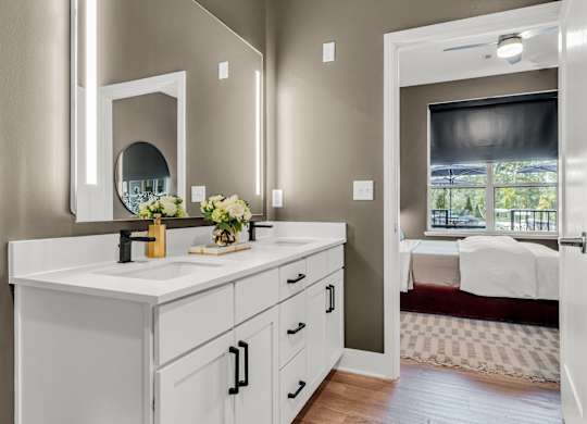 A bathroom with a vanity, mirror, and a bedroom in the background at Luxe 360 on Centerpointe Apartments, Virginia, 23114