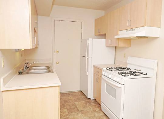 A gallery-style kitchen with a stove, sink, and refrigerator at Madeira Apartments in Kalamazoo, MI