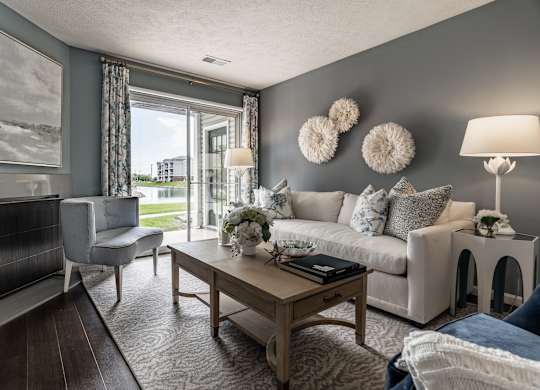 A living room with a white couch, a wooden coffee table, and a large window with a view of the outside at Mallard Bay Apartments, Crown Point, Indiana