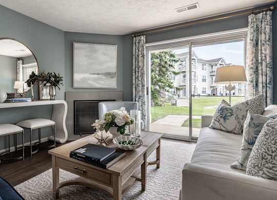 A living room with a sofa, a coffee table, a mirror, and a window with a view of a building at Mallard Bay Apartments, Crown Point, Indiana