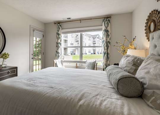 A bedroom with a large bed, a dresser, and a window with curtains at Mallard Bay Apartments, Crown Point, Indiana