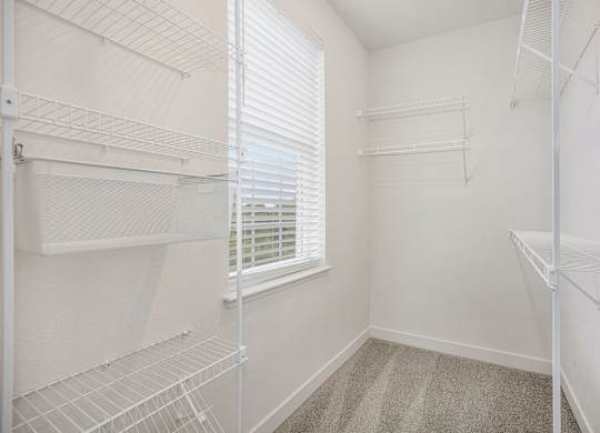 A white walk-in closet with shelves and a window with blinds at Meadowbrooke Apartment Homes in Kentwood, MI 49512