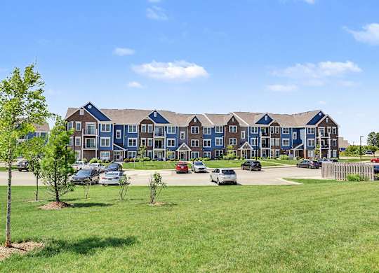 A large apartment building is surrounded by a grassy area and a few trees at Meadowbrooke Apartment Homes in Grand Rapids, MI 49512