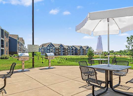 A grilling area with a table and chairs under an umbrella at Meadowbrooke Apartment Homes in Grand Rapids, MI 49512