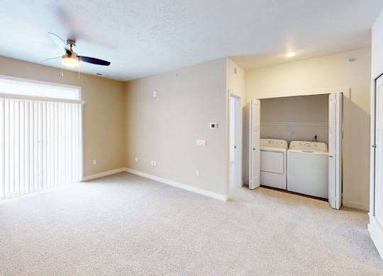 A living room with a ceiling fan and a closet with a washer and dryer inside at Meadowbrooke Apartment Homes in Kentwood, MI 49512
