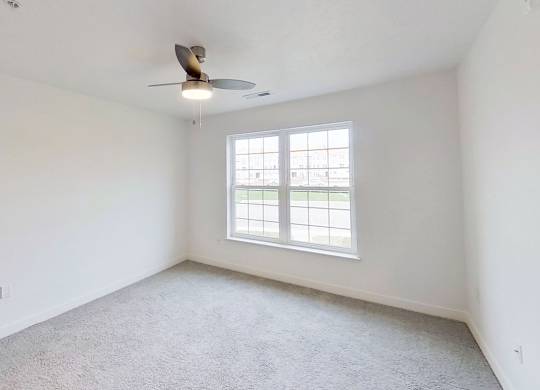 A bedroom with a ceiling fan and a large window at Meadowbrooke Apartment Homes in Kentwood, MI 49512
