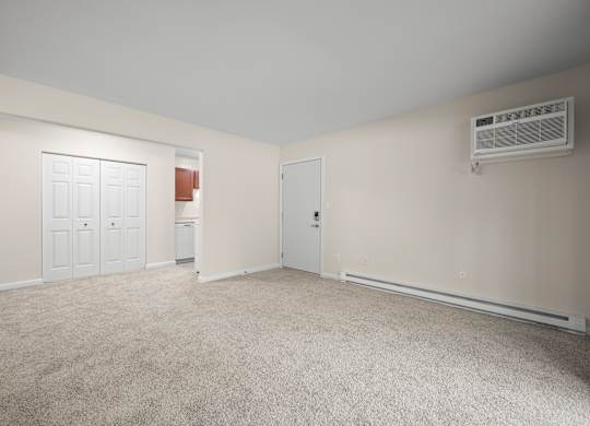 A room with a carpeted floor, two doors, and an air conditioning unit on the wallk at Timberlane Apartments, Peoria, Illinois