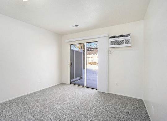 A bedroom with a grey carpet and a slider to a private patio at Newport Village Apartments, Portage, MI