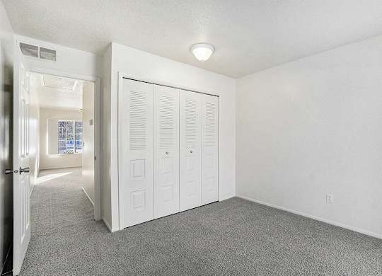A bedroom with a grey carpet and a closet at Newport Village Apartments, Portage, MI