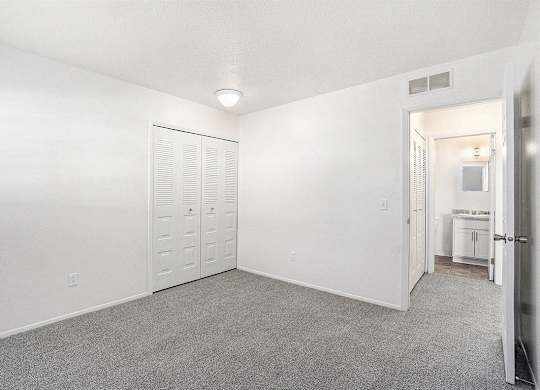 A spacious bedroom with a grey carpet and a closet at Newport Village Apartments, Portage, MI