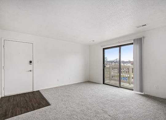 A living room with plush carpet and a slider to a private balcony with a view at Normandy Village Apartments, Michigan City, 46360