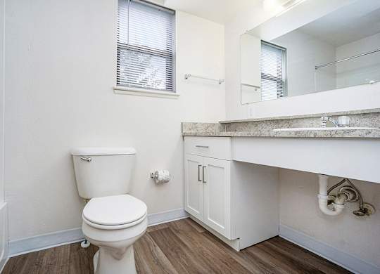 A white toilet sits in a bathroom with a window and white vanity at North Pointe Apartments in Elkhart, IN