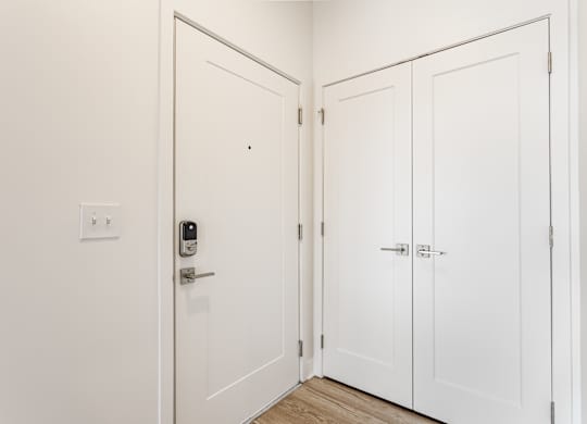 A white door with a keypad lock is open to a hallway with three white doors at Nuvo Flats, Indiana, 46410