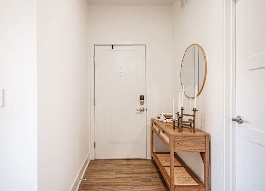 A white door is in a hallway with a wooden table and mirror in front of it.