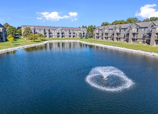 A fountain in the middle of a pond in back of apartment buildings at Oak Shores Apartments in Oak Creek, WI