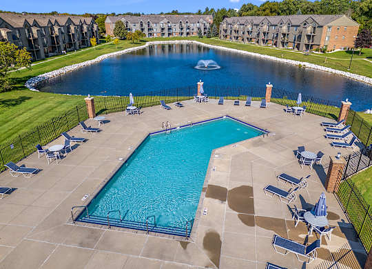 A large swimming pool surrounded by lounge chairs and a pond with a fountain behind it at Oak Shores Apartments, Wisconsin