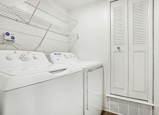 A white dryer and washing machine in a laundry room at Pine Knoll Apartments, Battle Creek