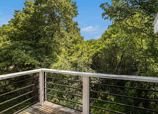 A balcony with a metal railing overlooks a wooded area at Pine Knoll Apartments, Battle Creek, 49014