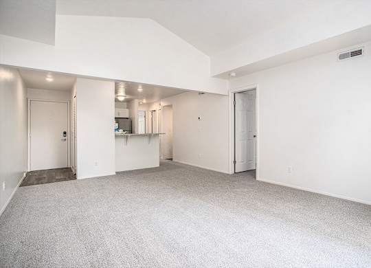 A large, empty living room with a cathedral ceiling and carpeted floor at Pine Knoll Apartments, Battle Creek, 49014