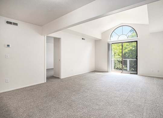A spacious living room with a large window, cathedral ceiling, and carpeted floor at Pine Knoll Apartments, Battle Creek, 49014