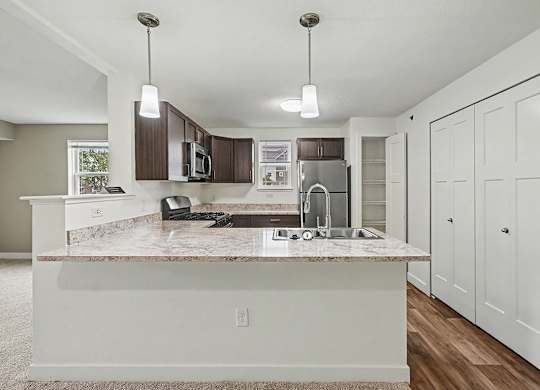 A kitchen with a breakfast bar and brown cabinets at The Reserve at The Reserve at Destination Pointe in Grimes, IA 50111