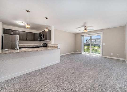 A spacious living room with a kitchen area and sliding glass doors leading to a balcony.