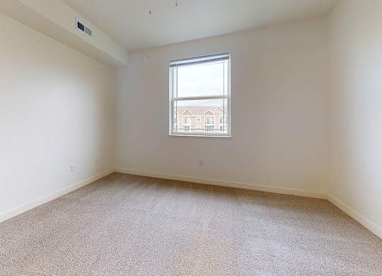 Empty bedroom with carpeted floor and a window at The Reserve at Destination Pointe apartments, Grimes, IA