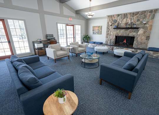A living room with a stone fireplace and a variety of seating options at Rivers Edge Apartments, Waterford, MI