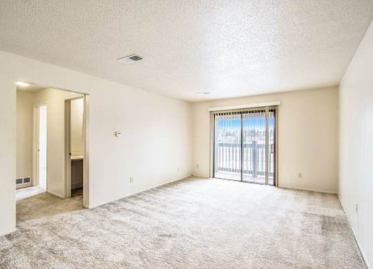 A spacious living room with a carpeted floor and a sliding glass door leading to a balcony at Seville Apartments, Kalamazoo, MI
