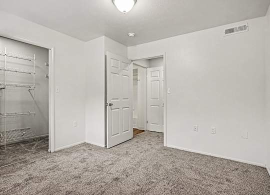 A white room with a carpeted floor and a white closet with shelves.