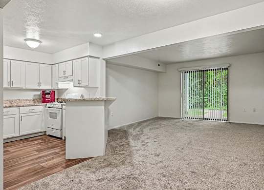A white kitchen with a window and a carpeted floor.