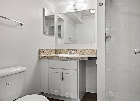 A white bathroom with a marble countertop and a toilet.