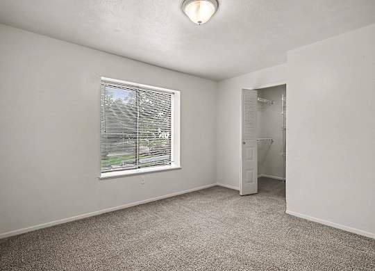 A room with a carpeted floor, a window with blinds, and a door leading to another room.
