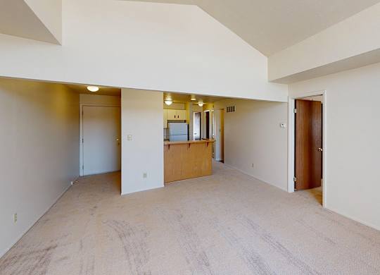 A large empty living room with a high ceiling and a kitchen with a breakfast bar at South Bridge Apartments in Fort Wayne, Indiana