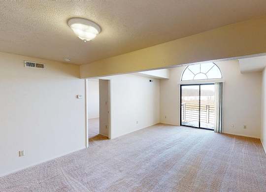 spacious living room with a cathedral ceiling and a door to a balcony at South Bridge Apartments in Fort Wayne, Indiana