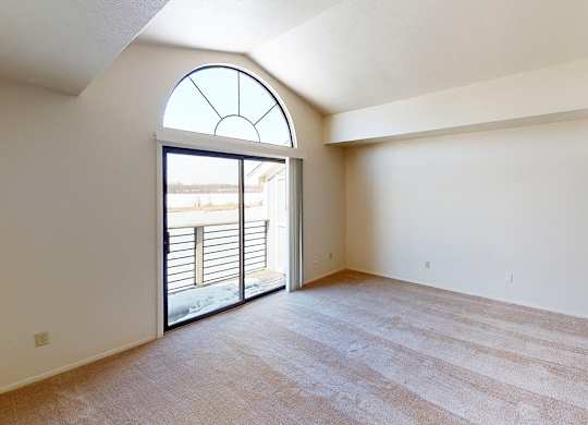 A living room with a cathedral ceiling and large window and sliding glass doors to a balcony at South Bridge Apartments in Fort Wayne, Indiana