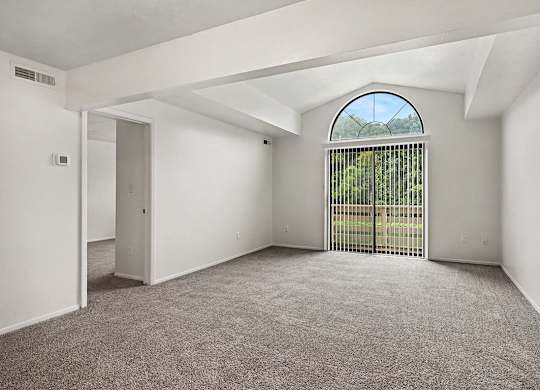 A room with a carpeted floor and a large window with a view of a fence and trees.