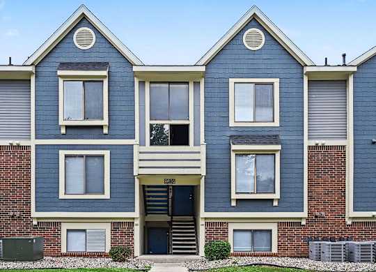 A blue and white two story apartment building with a black door and windows.