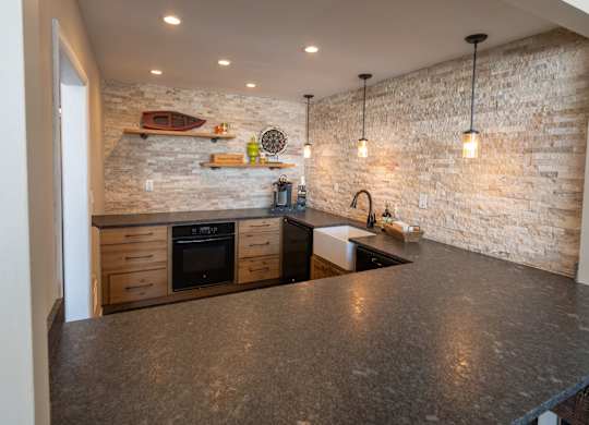 A kitchen with a stone wall and a black counter top.
