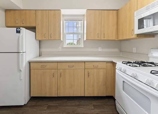 A kitchen with window, wooden cabinets and white appliances at Stoney Pointe Apartment Homes, Kansas