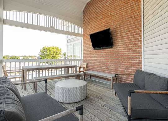 A balcony with a grey couch, a white ottoman and a flat screen TV mounted on a brick wall. at Sundance Apartments, Indianapolis, IN
