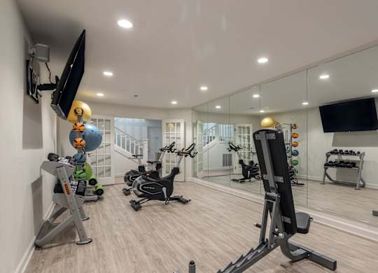 A well-equipped home gym with various exercise machines and a flat-screen TV mounted on the wall. at Sundance Apartments, Indiana