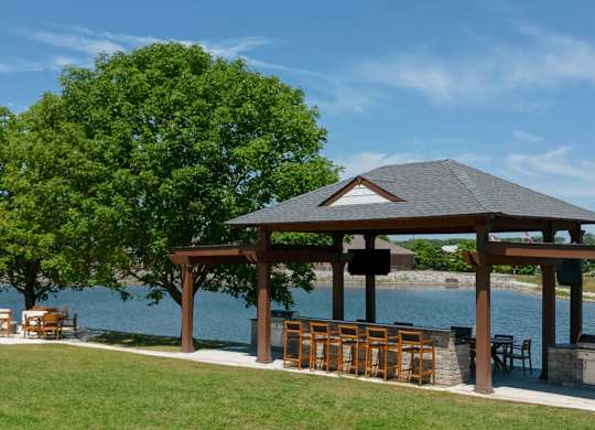 A gazebo with a table and chairs is situated on a lawn by a body of water. at Sundance Apartments, Indianapolis, IN