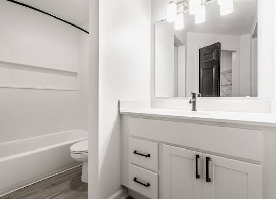 A white bathroom with a tub, sink, and mirror. at Sundance Apartments, Indianapolis