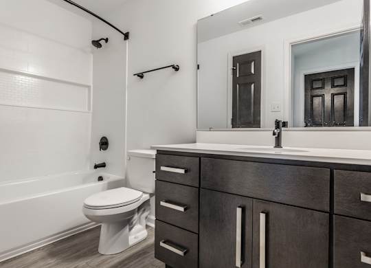 A white toilet sits in a bathroom with a wooden vanity and a large mirror. at Sundance Apartments, Indiana