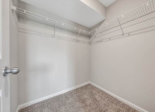A white door is on the left of a room with a carpeted floor and a wall with a metal shelf. at Sunscape Apartments, Virginia