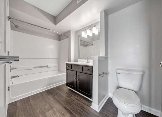 A white toilet sits in a bathroom with a wooden floor and white walls. at Sunscape Apartments, Roanoke, 24018