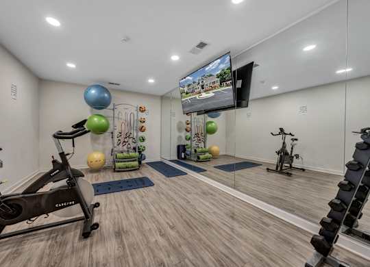 A home gym with a variety of exercise equipment including a stationary bike, a treadmill, and a television mounted on the wall. at Sunscape Apartments, Virginia