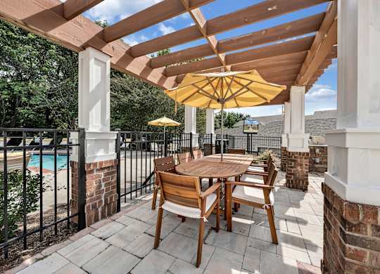 A wooden table and chairs are set up on a patio with a yellow umbrella. at Sunscape Apartments, Roanoke, Virginia